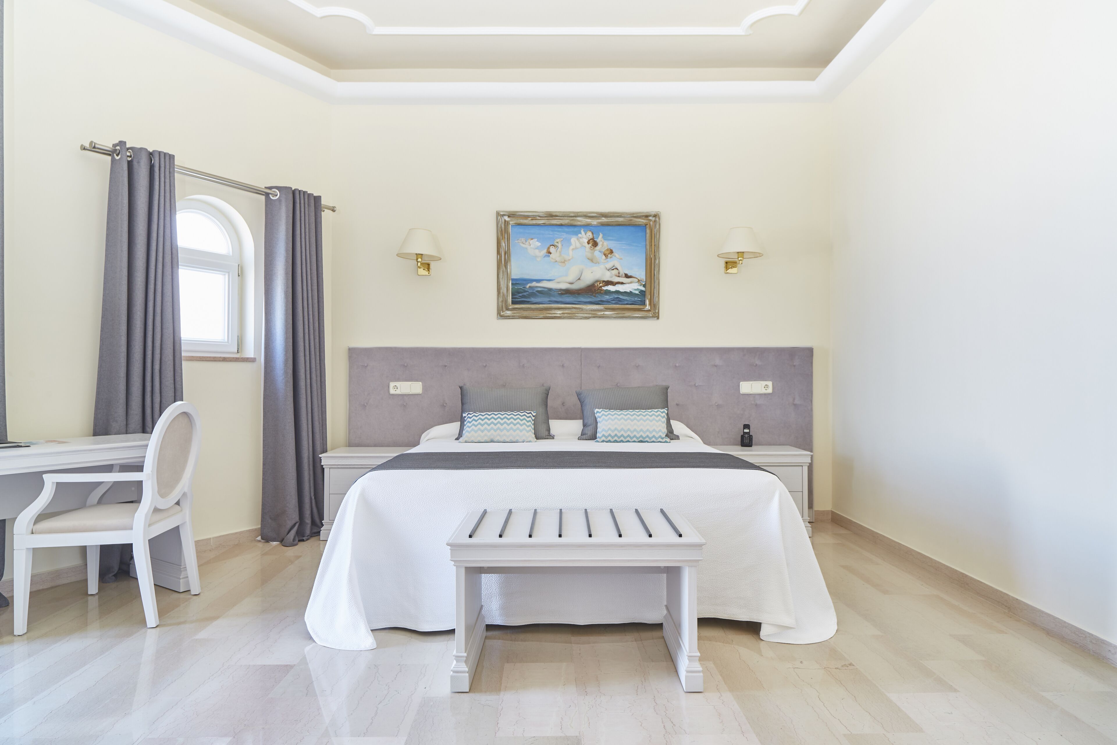 A bedroom with a bed, a desk, a chair, a bench, a window with curtains, and wall-mounted lamps.