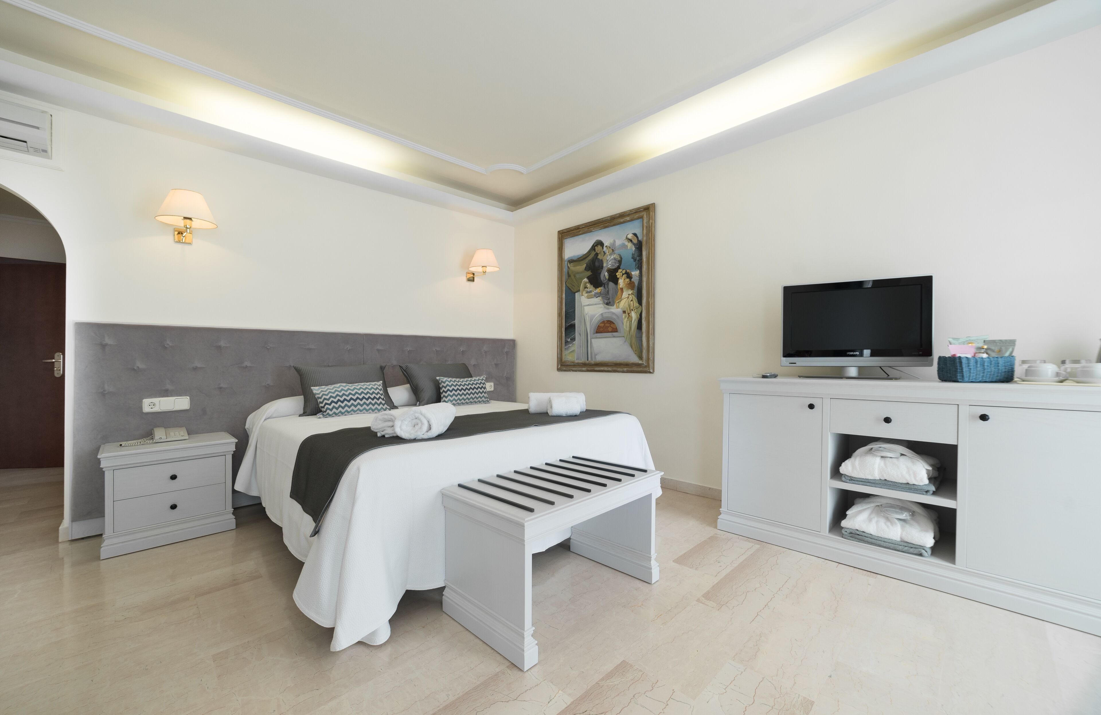 Een moderne slaapkamer met een bed, nachtkastjes, een bankje, een televisie en een schilderij aan de muur.