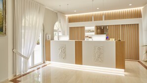Un área de recepción de diseño moderno, con mostrador de recepción, un ventanal grande con cortinas translúcidas y un panel de pared de madera.