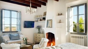 A cozy bedroom with a fireplace, a bed, a window with a view, a TV, and a bookshelf. - Villa Station Las Salinas (Ses Salines)
