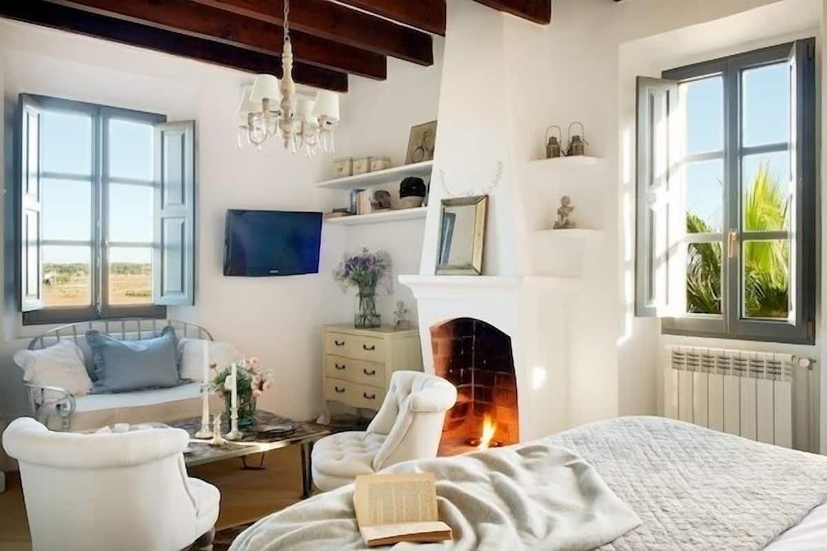Ein gemütliches Schlafzimmer mit Kamin, Bett, Fenster mit Blick und Bücherregal.
