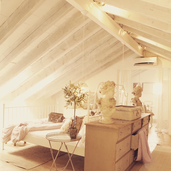 A spacious attic bedroom with a sloped ceiling, a bed, a dresser, and a small table with a plant. - Villa Station Las Salinas (Ses Salines)