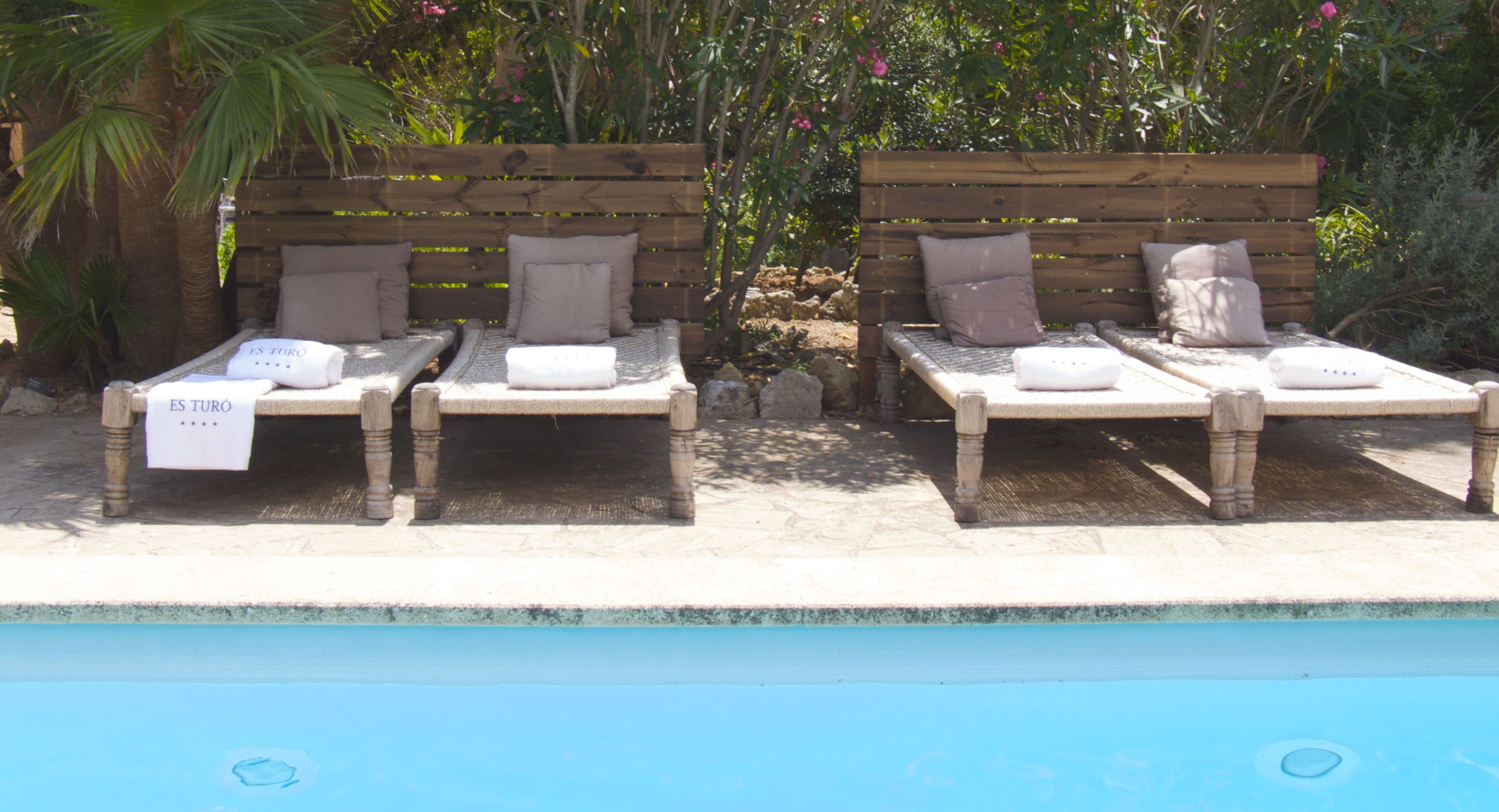Dos sillones de madera con toallas y almohadas, ubicados junto a una piscina.