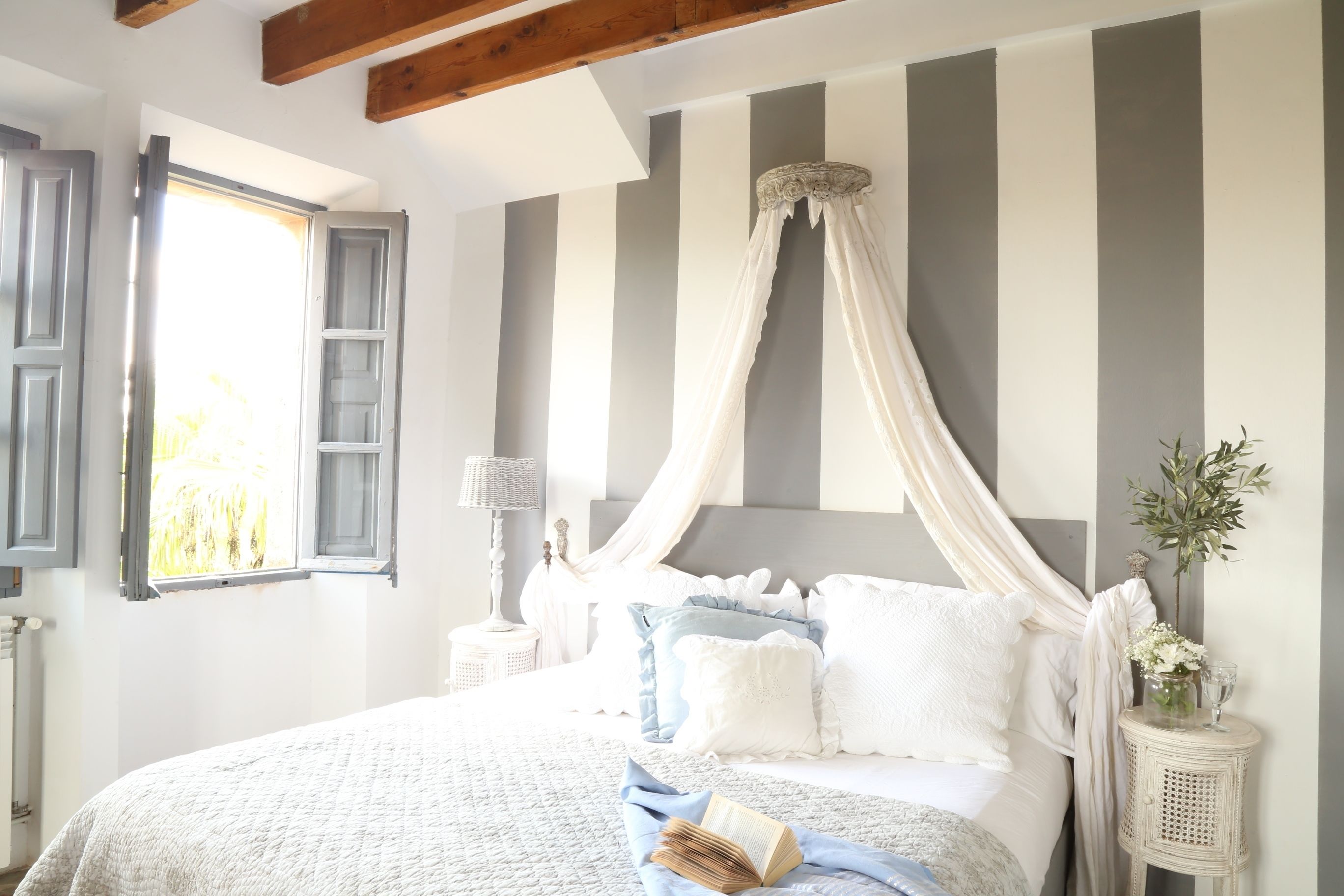 Un dormitorio con una cama, una mesita de noche, una lámpara y un ventanal con cortinas.