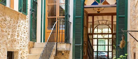 A stone staircase leading to a wooden door with green shutters, a small bench, and potted plants.