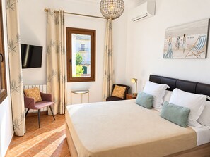 Een hotelkamer met een groot bed, een televisie, een tafeltje, een stoel en een schilderij aan de muur.