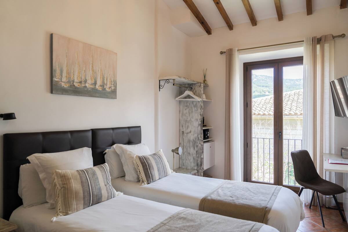 Une chambre d’hôtel avec deux lits, un tableau, une armoire, un bureau et une vue sur l’extérieur.