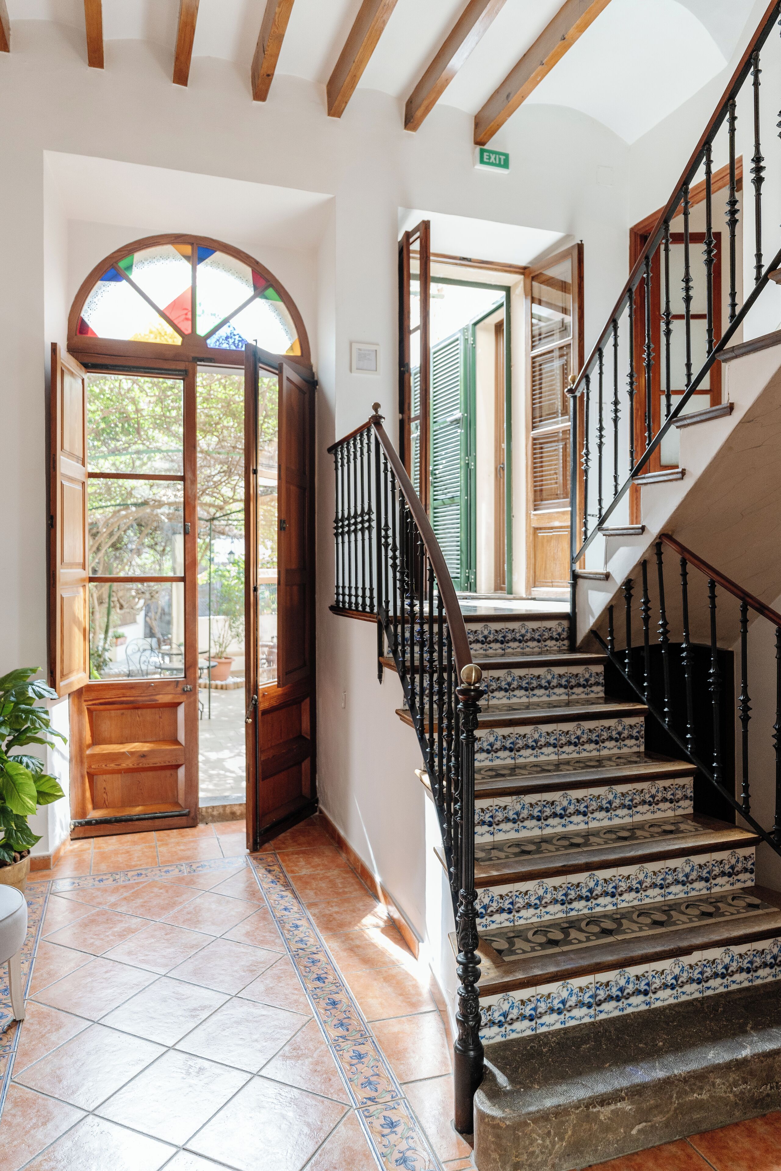 Uma escadaria com grades pretas ornamentadas e azulejos estampados que levam a uma área externa.