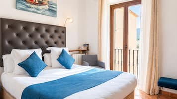 Een slaapkamer met een groot bed, een hoofdeinde, een nachtkastje met boeken, een stoel en uitzicht op de omgeving via een balkondeur.