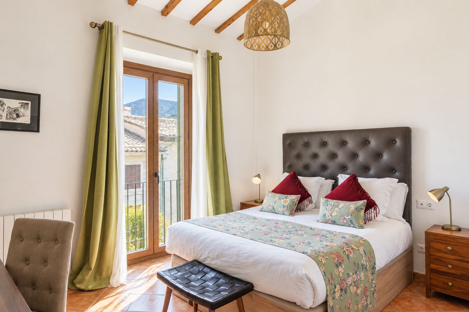 A bedroom with a large bed, a chair, a nightstand, a lamp, and a view of the outside.