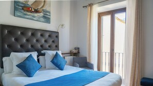 Un lit bien fait, doté d’une tête de lit capitonnée, d’un plaid bleu et de coussins assortis. On aperçoit une petite table d’appoint avec une lampe et des livres.