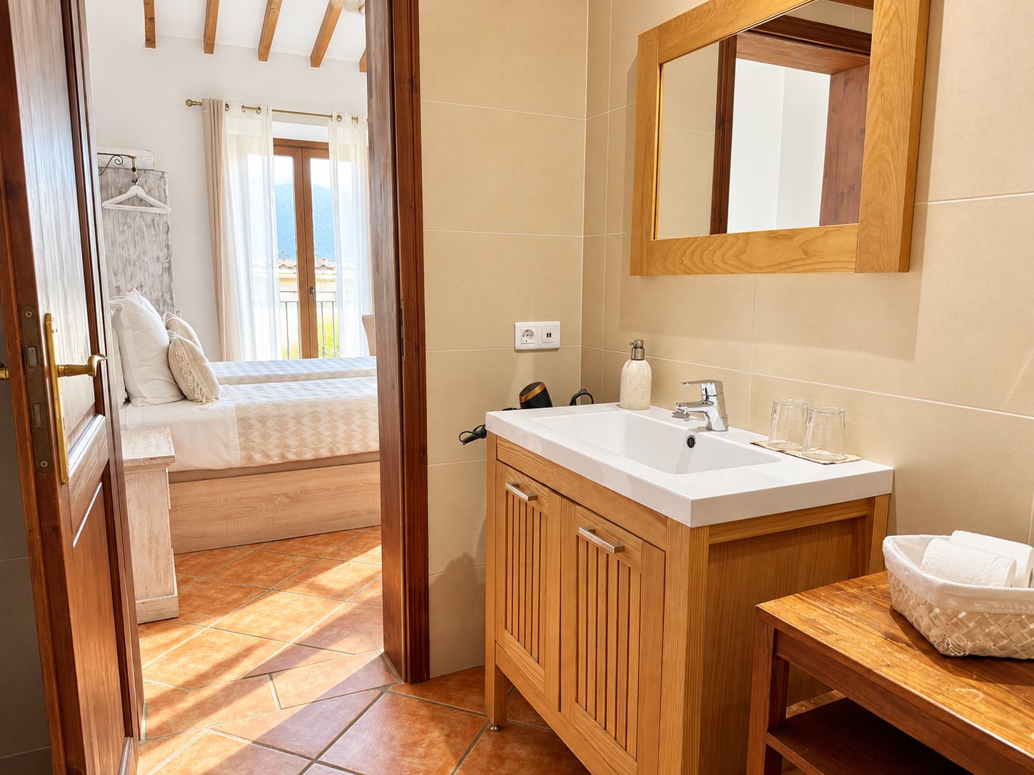 Habitación de hotel con cama de madera, un gran ventanal con cortinas, tocador de madera con lavabo y un espejo.