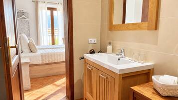 Habitación de hotel con cama de madera, un gran ventanal con cortinas, tocador de madera con lavabo y un espejo.