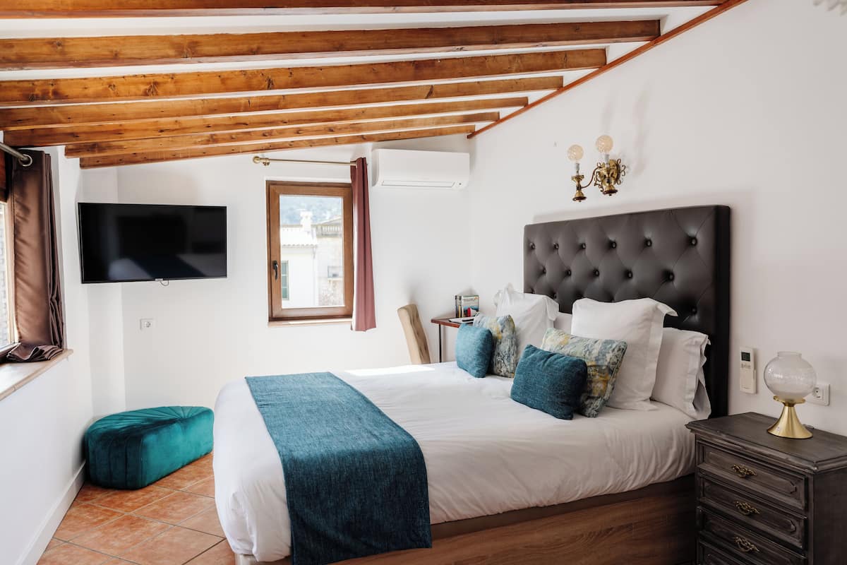 Une chambre avec un grand lit, un téléviseur fixé au mur, une fenêtre avec des rideaux et un plafond en bois.