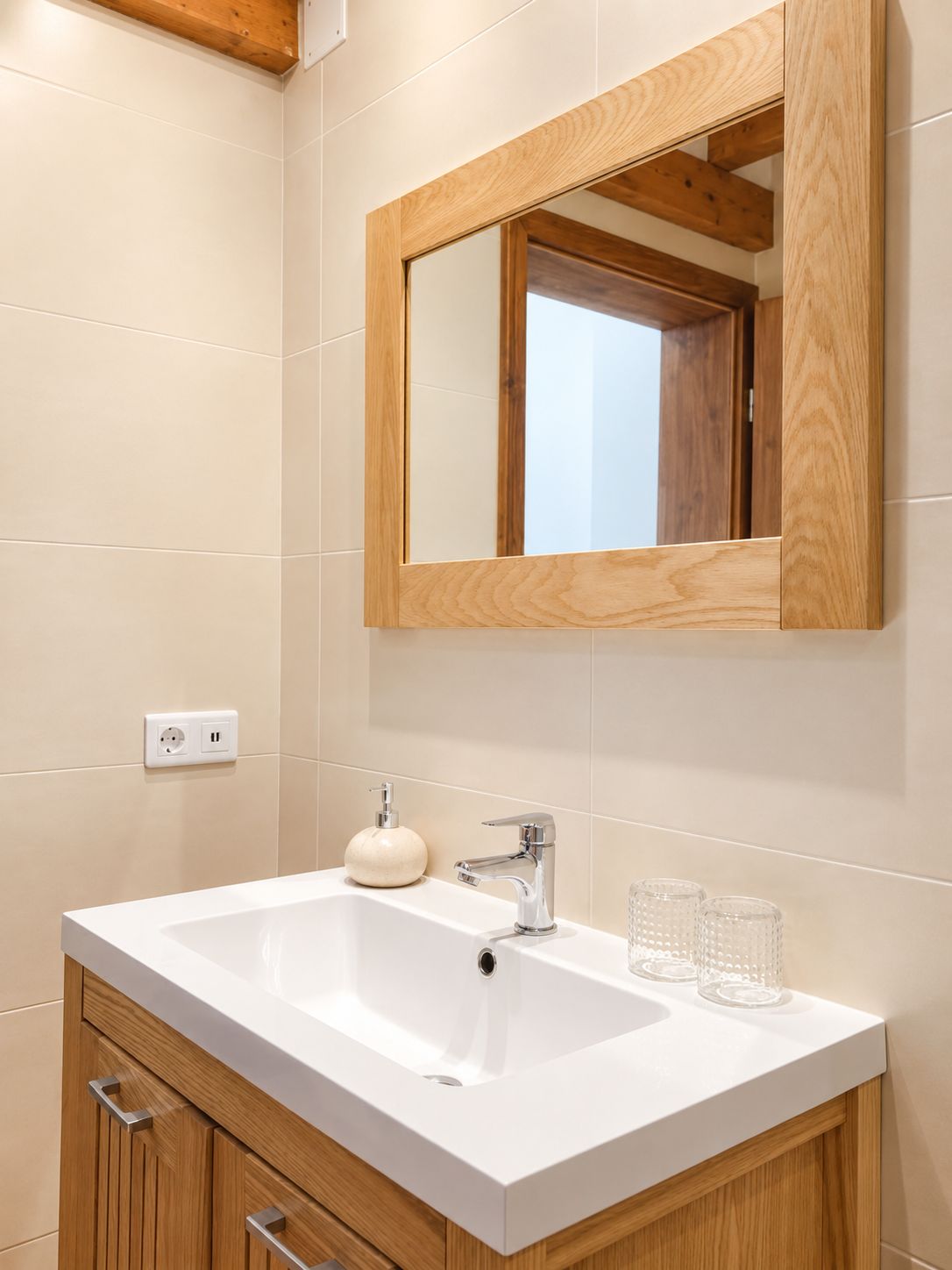 A modern bathroom with a white sink, wooden cabinet, and a mirror with a wooden frame.