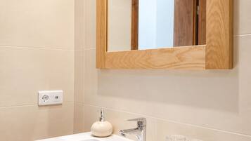 A modern bathroom with a white sink, wooden cabinet, and a mirror with a wooden frame.
