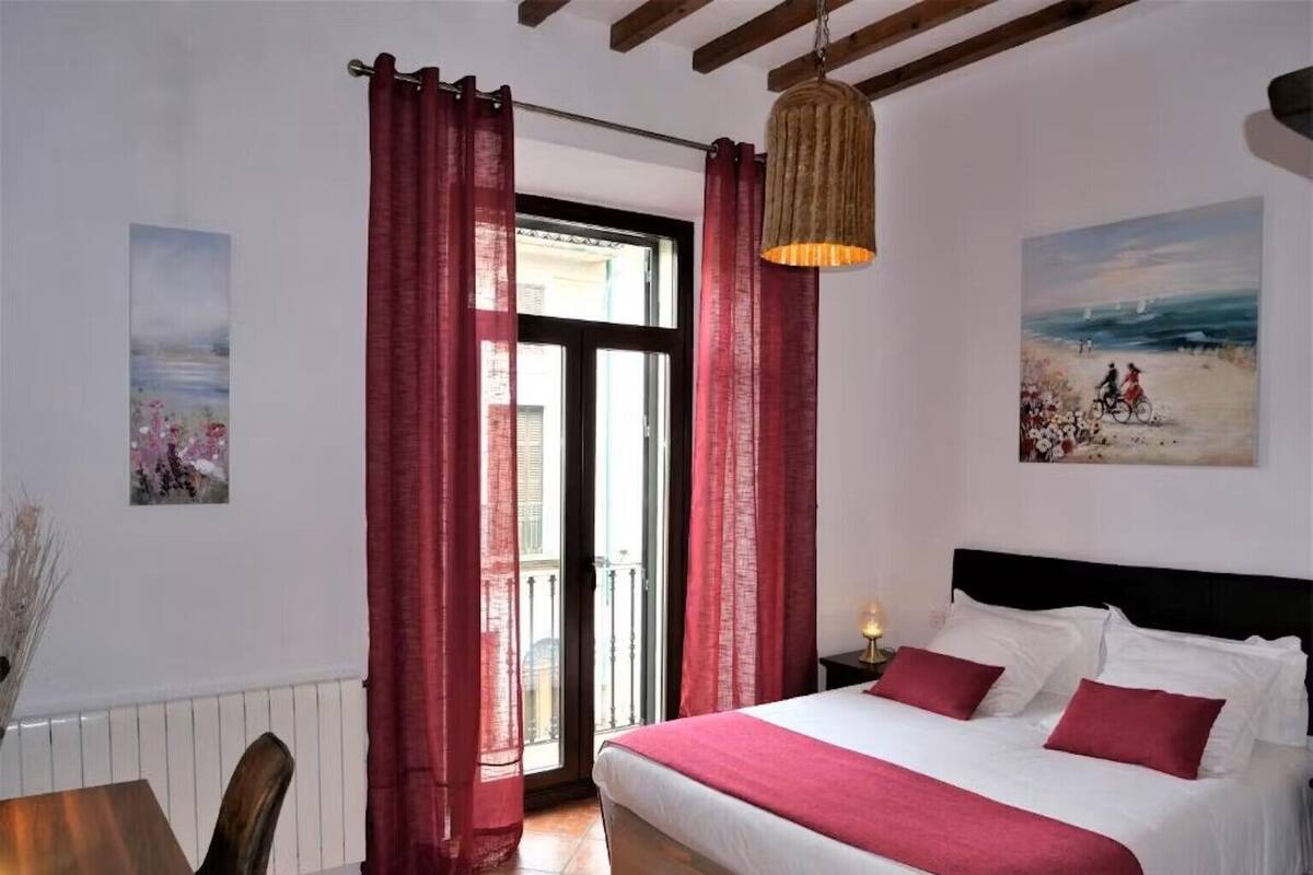 Une chambre à coucher avec un lit, des rideaux rouges, un luminaire suspendu et un tableau accroché au mur.