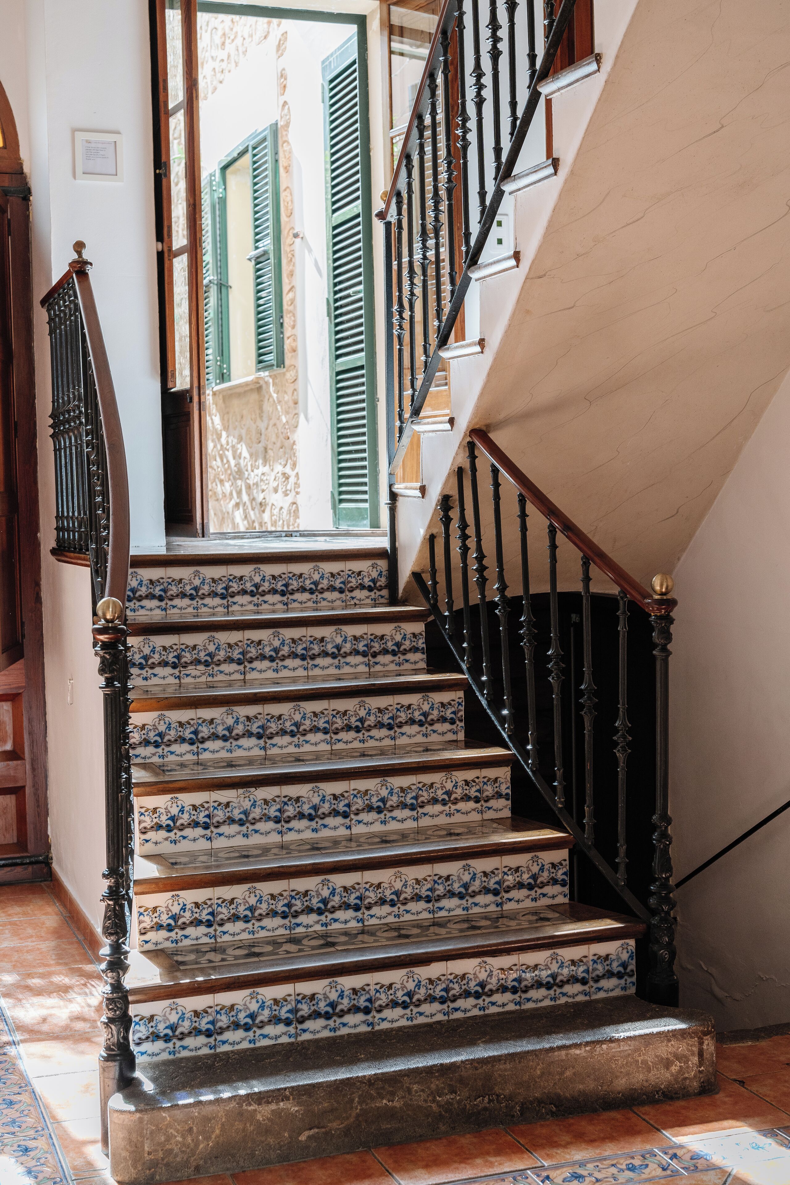 A staircase with blue and white patterned tiles, a wooden handrail, and a black iron railing.