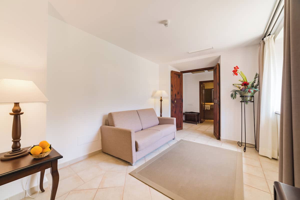 A living room with a beige sofa, a small table with a lamp, and a vase with flowers.