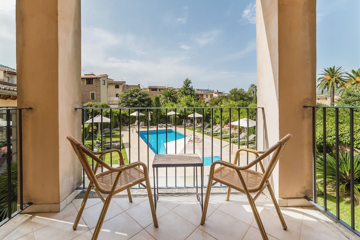 A balcony with two wicker chairs and a small table, overlooking a swimming pool and lush greenery.