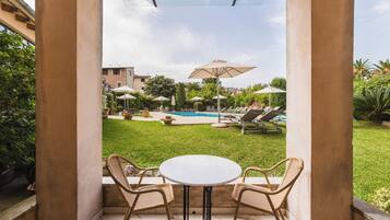 A patio with a round table and wicker chairs, overlooking a swimming pool area with lounge chairs and umbrellas.