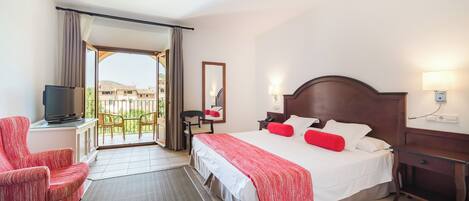 A hotel room with a bed, a desk, a chair, a TV, and a balcony with a view of buildings.