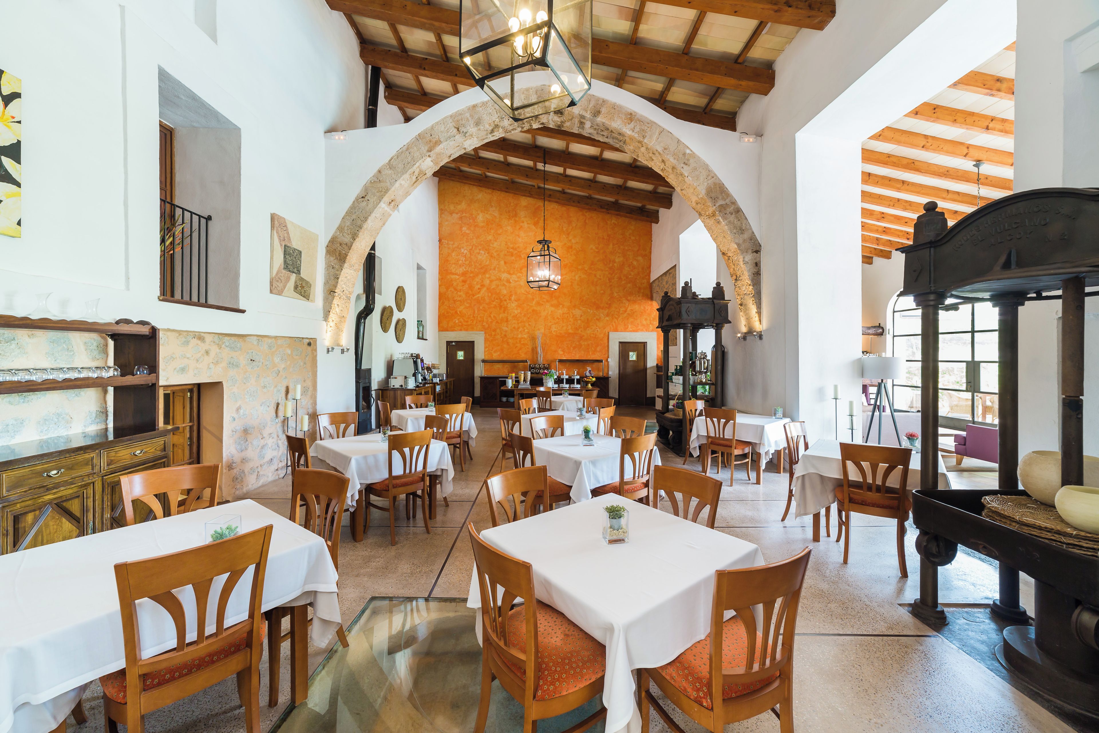 Een restaurant met meerdere tafels en stoelen, een gewelfde stenen muur en een houten plafond.