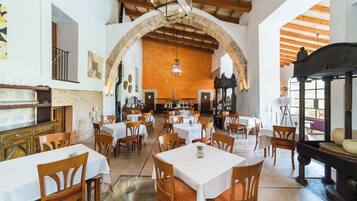 Un restaurante con varias mesas y sillas, un muro de piedra con arco y un techo de madera.