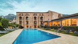 Une piscine avec des chaises longues, un bâtiment doté de nombreux balcons et une chaîne de montagnes en arrière-plan.