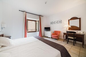 A hotel room with a bed, a desk with a chair, a television, and a window with curtains.
