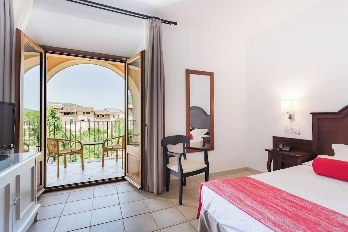 A hotel room with a balcony, a bed, a chair, a desk, and a TV.