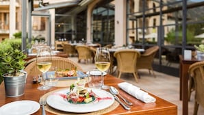 Un espace extérieur aménagé pour les repas, avec des tables, des chaises et une vue sur le bâtiment situé à l’arrière.