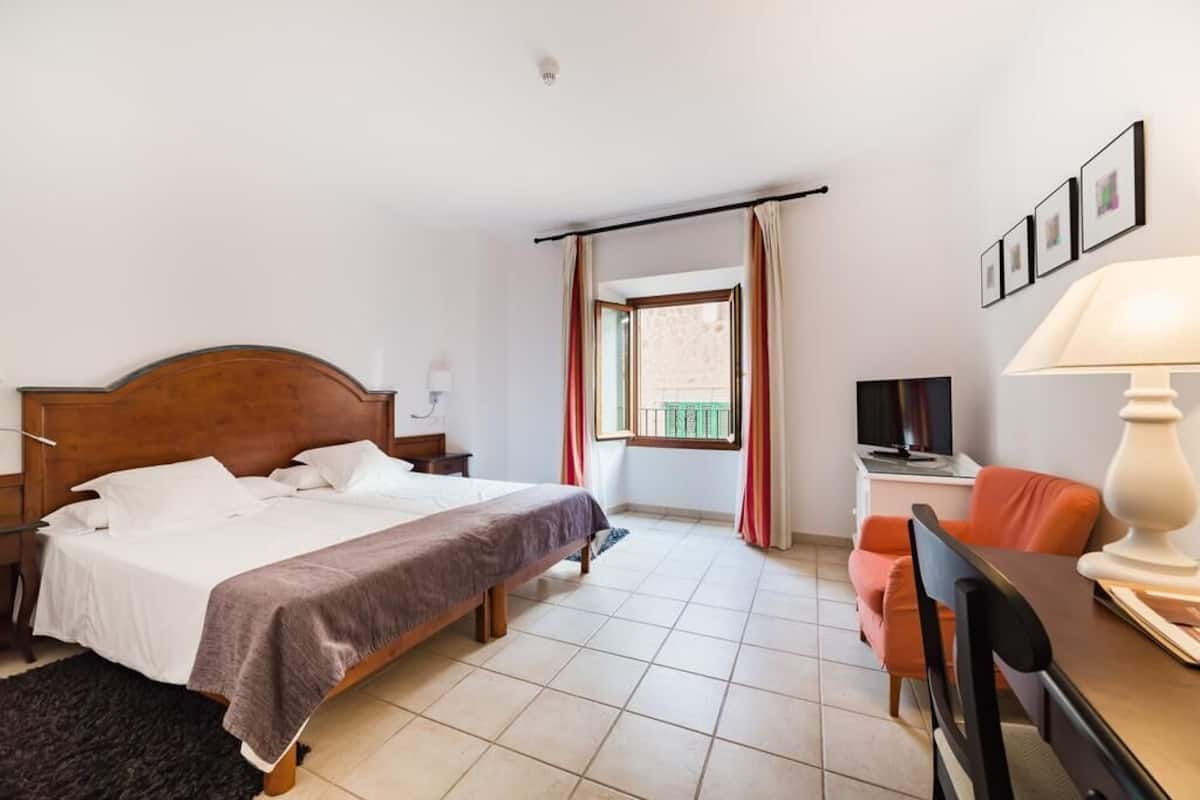 A hotel room with a wooden bed, a desk with a lamp, a chair, and a TV.