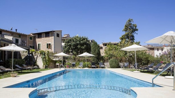 Una piscina con sillas de descanso y sombrillas, rodeada de edificios y árboles.