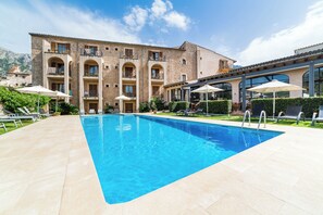 A swimming pool with lounge chairs and umbrellas, surrounded by a building with stone walls and multiple balconies. - Ca'l Bisbe (Sóller)