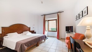 Una habitación de hotel con cama, escritorio, silla, televisor y ventana con cortinas.