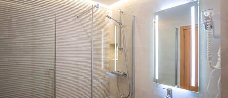 A modern bathroom with a glass shower enclosure, a large mirror, and a sink with a towel.