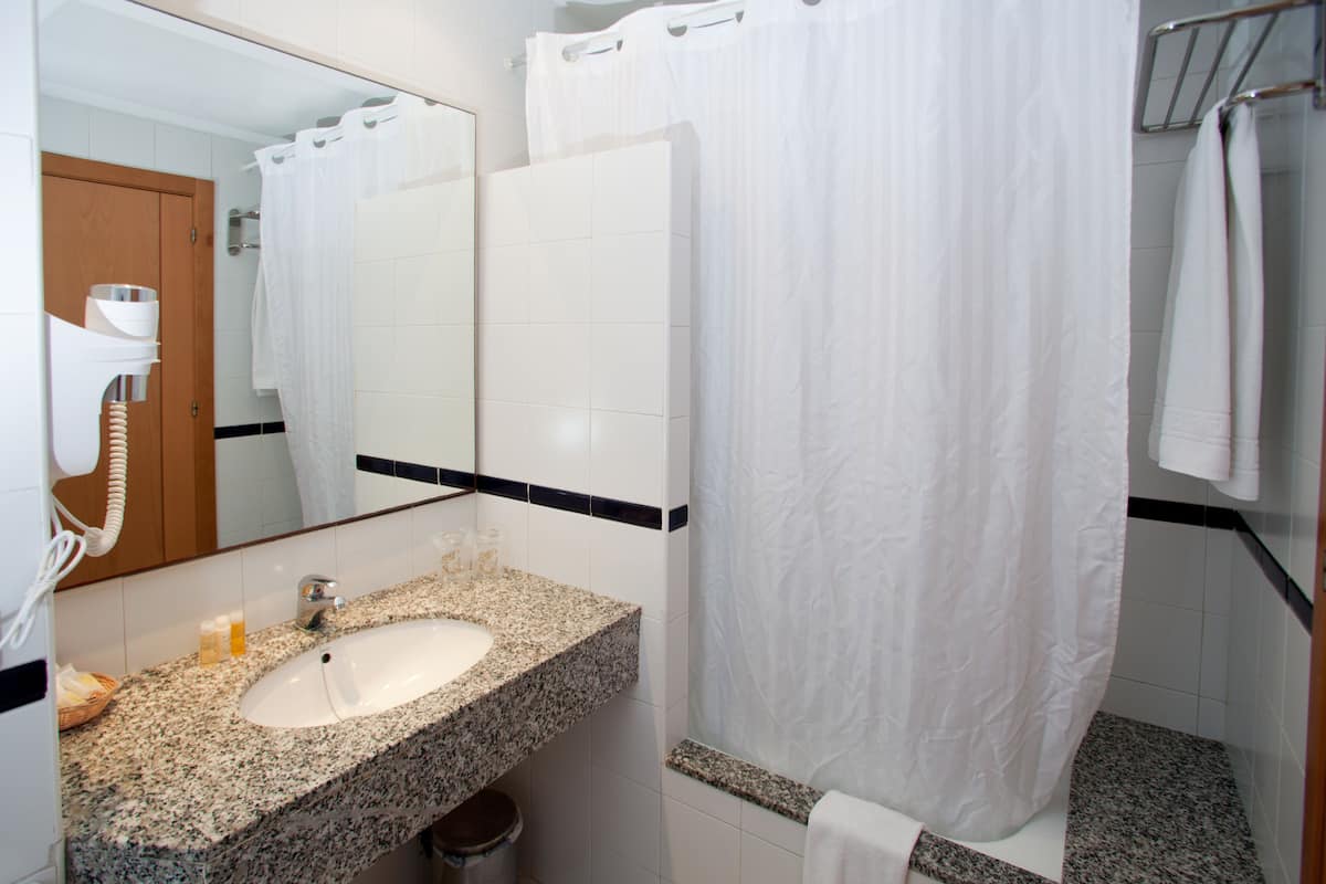 Un bagno con lavabo su piano in granito, uno specchio, una tenda da doccia e un portascopevoli.