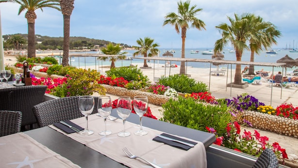 A table set for dining with a view of the beach and boats. - Hotel Ses Figueres (Ibiza Town)