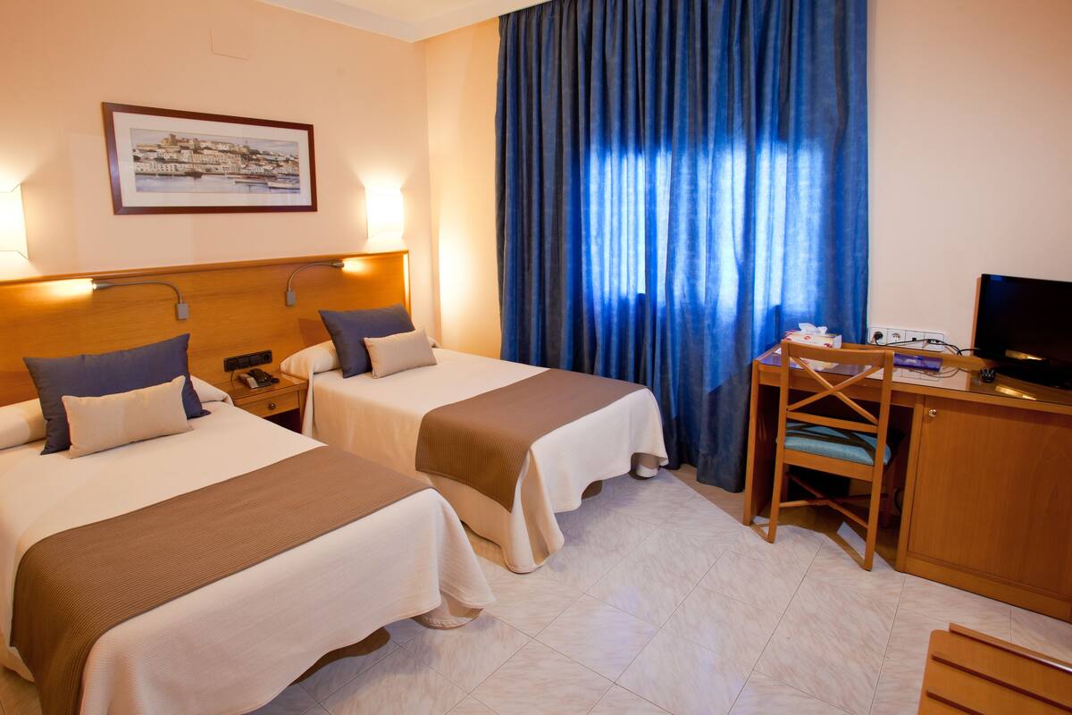 Una camera d'albergo con due letti, una scrivania, una sedia, una televisione e un quadro appeso al muro.