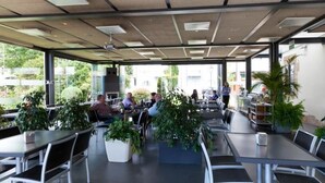 An outdoor dining area with tables and chairs, surrounded by potted plants and large windows offering views of the outdoors. - La Casa del Patrón (Zuia)
