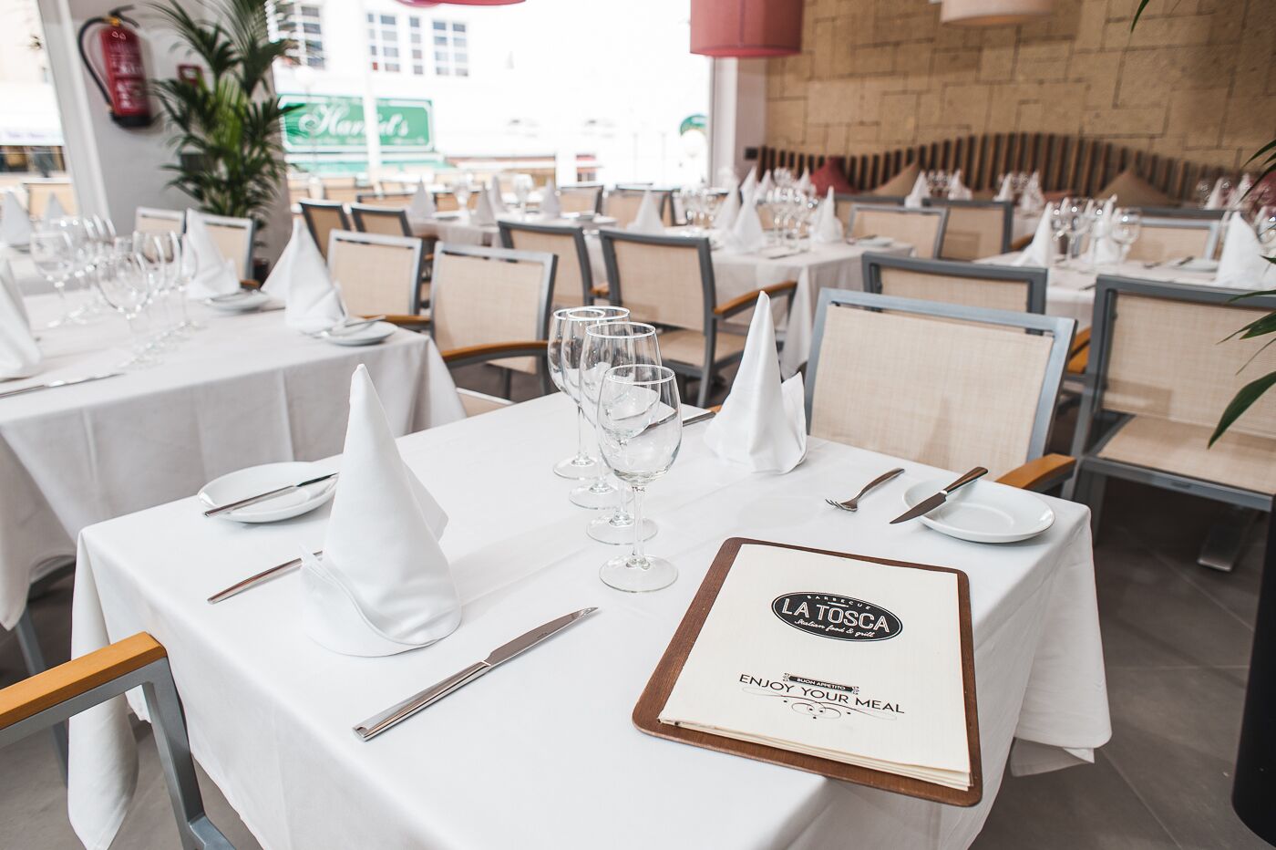 En restaurantscene med borde dækket til spisning, hvide dugge, pænt anrettet bestik og vinglas.