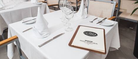 A restaurant setting with tables set for dining, featuring white tablecloths, neatly arranged cutlery, and wine glasses.