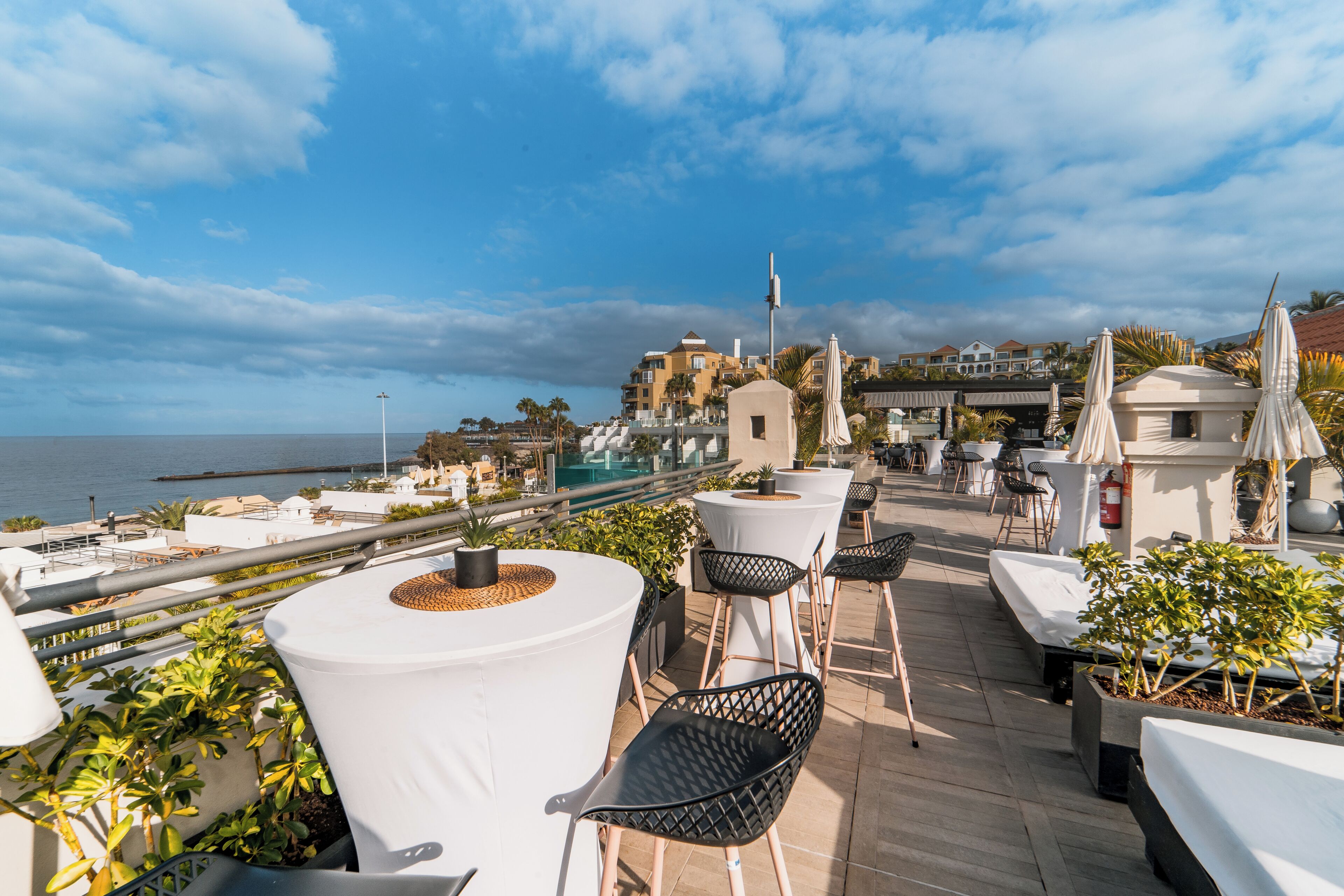 A rooftop terrace with outdoor seating, a view of the sea, and buildings in the background.