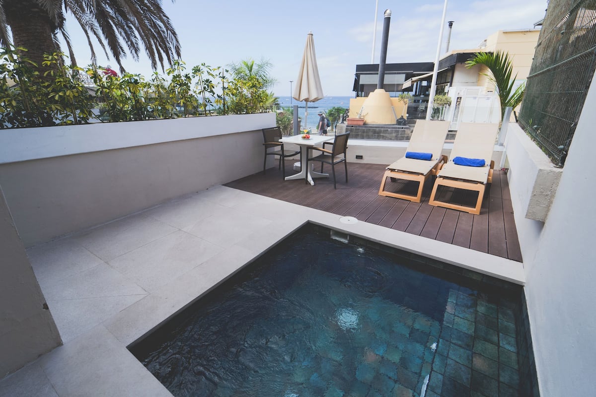 A rooftop pool area with a table and chairs, a small pool, and a view of the ocean.