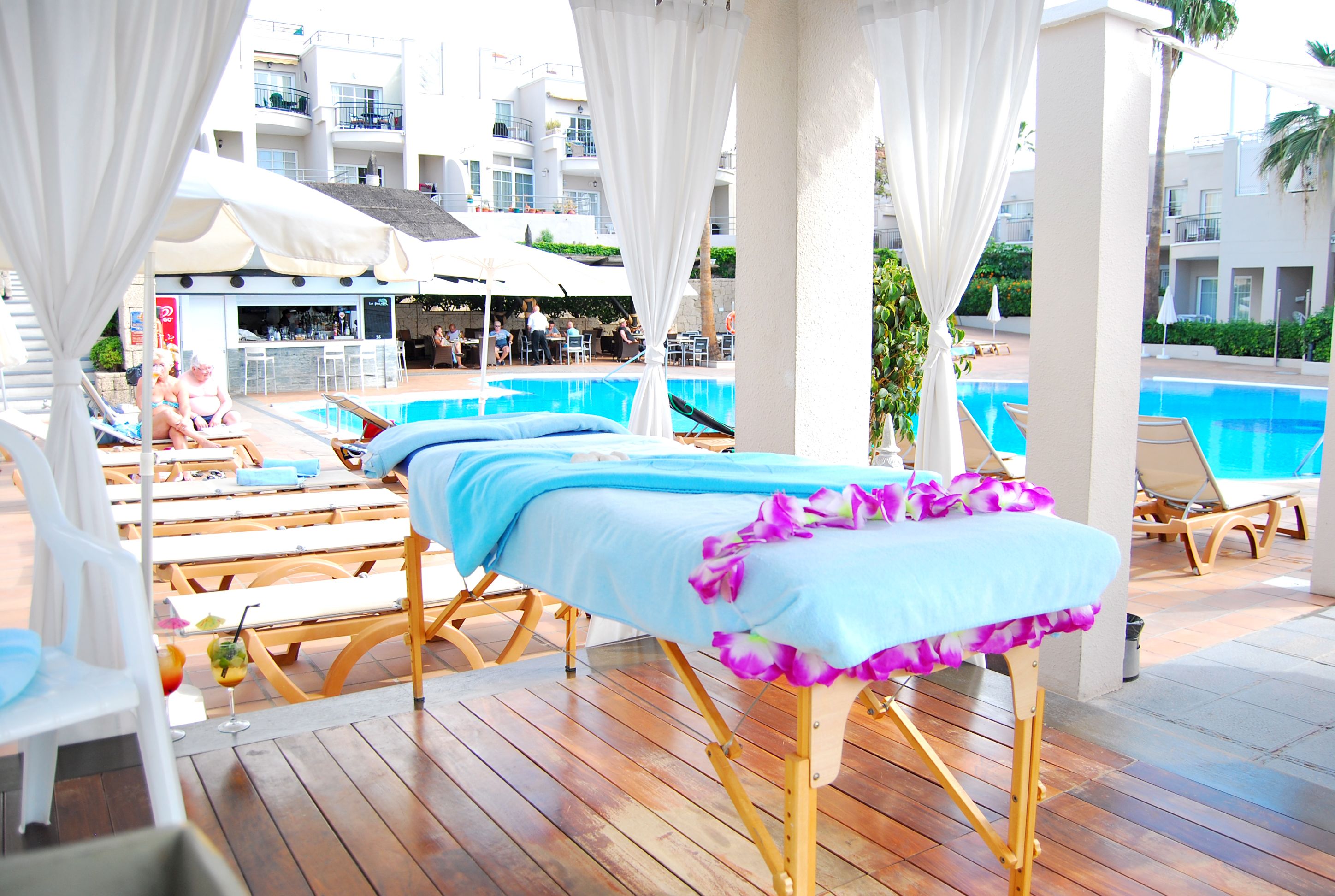 Ein Poolbereich mit Liegestühlen, einer Massageliege und einer Bar im Hintergrund.