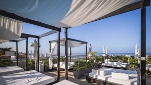 Een dakterras met witte zachte zitplaatsen, potplanten en uitzicht op zee.