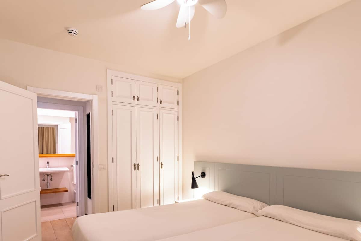 A bedroom with a bed, a ceiling fan, a wardrobe, and a bathroom visible through an open door.