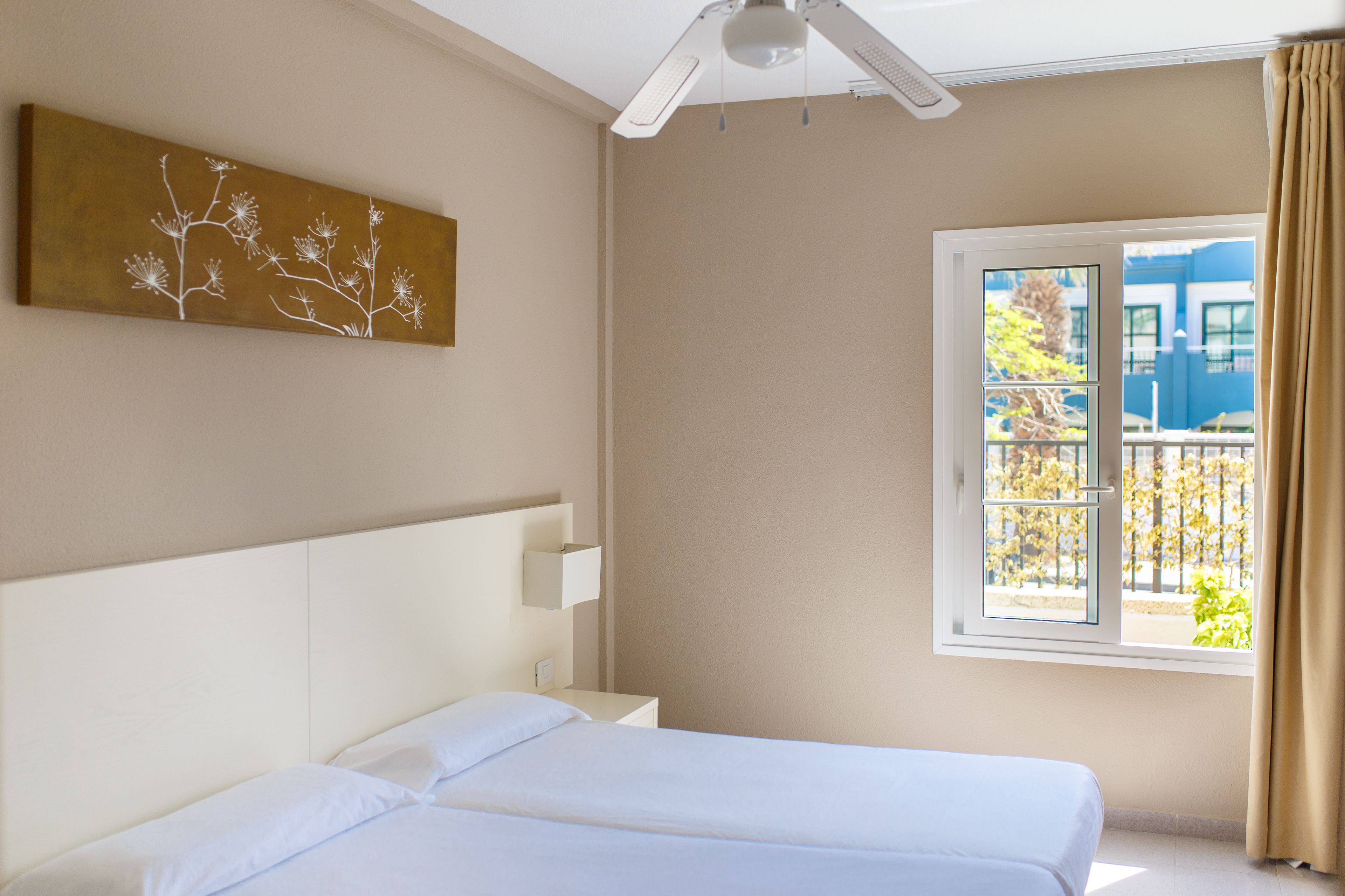 Une chambre d’hôtel avec un lit, une table de chevet, une œuvre d’art accrochée au mur et une fenêtre donnant sur des immeubles et des arbres.
