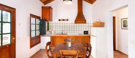 A kitchen with a wooden table, chairs, a white refrigerator, and a hanging light fixture.